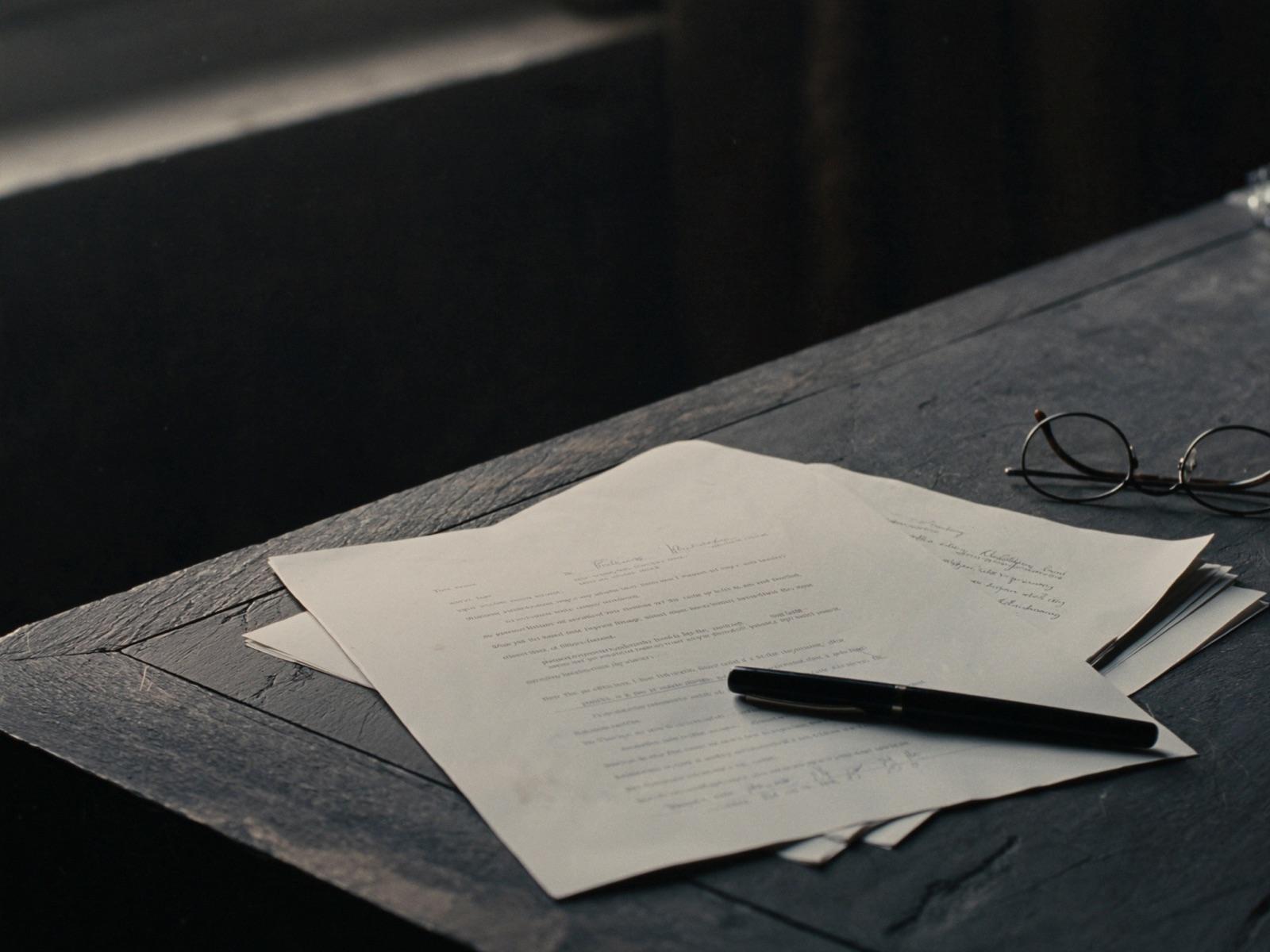 Les pages imprimées d'un contrat en éventail sur un bureau sombre, un stylo plume posé dessus.